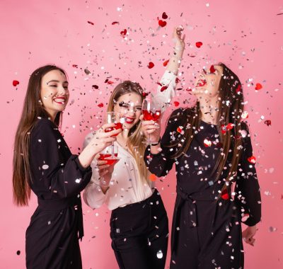 Girls posing and smiling on pink background, cheerful emotions, bright makeup, red lips, indoors party, wearing black and white stylish evening outfits.